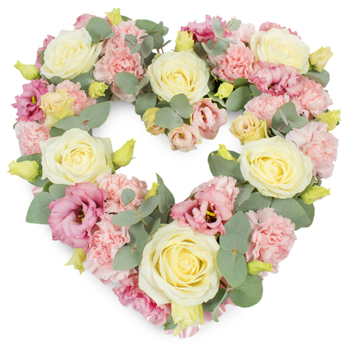 This image shows a meticulously crafted, heart-shaped funeral wreath set against a pristine white backdrop, allowing every bloom and leaf to stand out with quiet clarity. The heart is fully formed, with no gaps, its outline traced by a tapestry of cream and soft yellow roses that act as the primary focal points. Each rose is in full bloom, petals layered in tight spirals that gradually loosen toward the edges, giving a sense of fullness and gentle movement. Interspersed among these classical roses are clusters of pastel pink carnations, their frilled, almost feathered petals filling any remaining spaces so that the arrangement feels lush and generous from every angle. Richer tones are introduced by lisianthus flowers in magenta-pink and mauve shades, their softer, more open petals offering a contrast in shape and texture, as if small, delicate cups are cradling the memory of a loved one. Eucalyptus foliage, in muted silvery-green, winds gracefully throughout the heart, some leaves overlapping the petals, others peeking from behind, creating depth and a natural, garden-like feel reminiscent of quiet paths around Earlsfield's local green spaces. Tiny yellow-green buds are dotted here and there, subtle but intentional, suggesting new growth and the quiet resilience of those left behind. The design appears expertly balanced, with colour and shape distributed evenly so the eye naturally follows the heart's curve. It evokes the kind of comforting, dignified tribute many families choose for funeral and memorial services in and around Earlsfield, whether placed beside a photograph at a chapel, resting by a graveside, or delivered to a home gathering where friends and relatives share stories and hold each other close.
